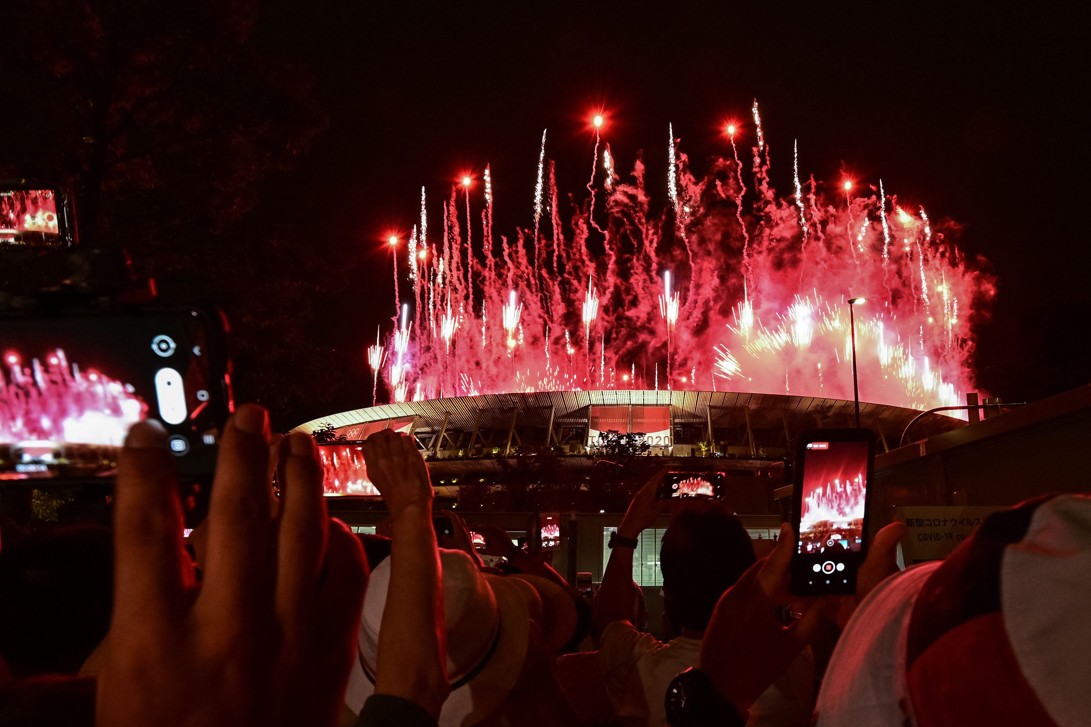 东京奥运开幕式上的烟花照亮了夜空，尽管本届奥运会开幕式禁止观众入场，但民众仍在体育场外拿起手机与相机，拍下这历史性的一刻。（法新社照片）