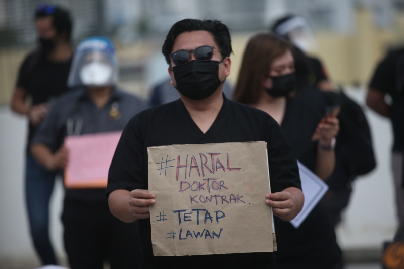 一名身穿黑衣，带黑色口罩的合约医生手持”合约医生罢工 （#Hartal Doktor Kontrak），继续抗争“纸卡参与隆中央医院罢工行动。