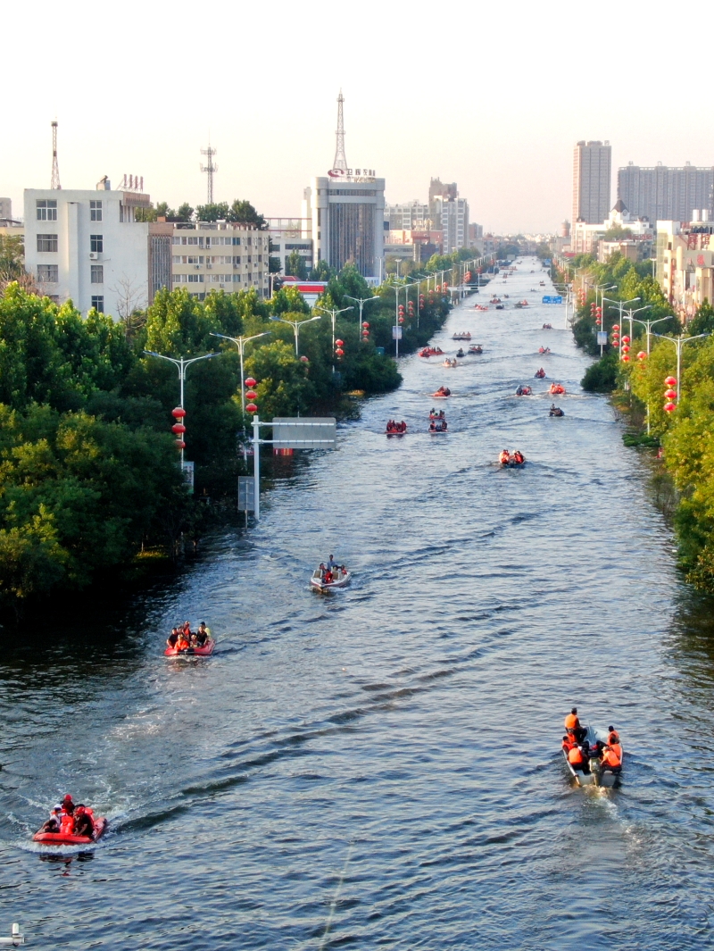 暴雨后，河南省卫辉市新乡昔日道路边一片汪洋，救援人员乘坐皮划艇在“水”路上救援被困病患及家属人员。