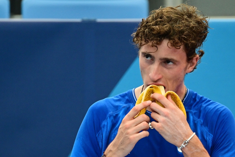 法国网球选手Frances Ugo Humbert在东京奥运会八强比赛休息时吃香蕉补充体力。（法新社照片）