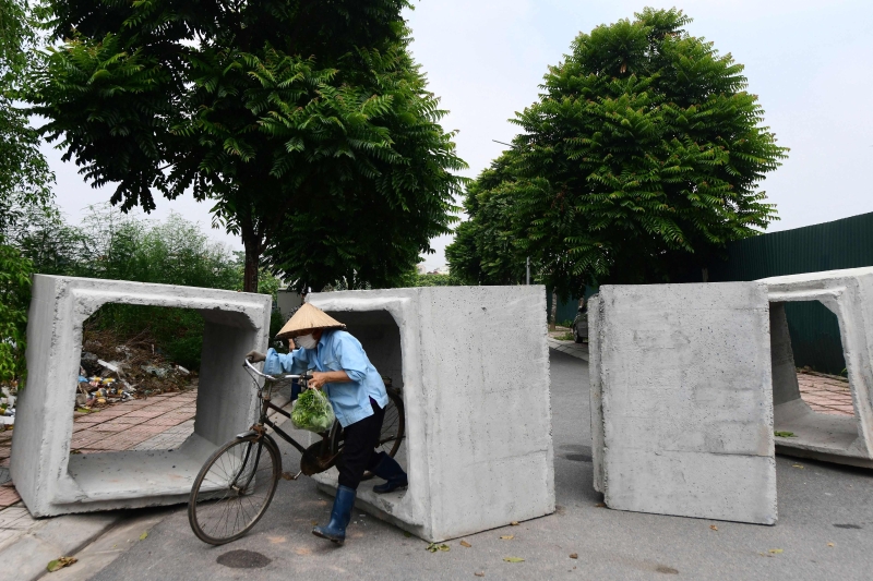 越南政府为了阻断冠病病毒的传播而实施两周的封锁，图为河内一名商贩为了生计，不顾禁令穿过混凝土巨石组成的临时路障。（法新社照片）
