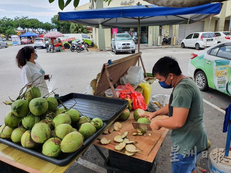 从事建筑业的陈智勇（右）当起椰子摊贩，继续用自己的双手赚取生活收入。