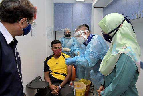 阿汉峇峇（右二）向接种者展示疫苗及针筒里的疫苗剂量。（马新社图）